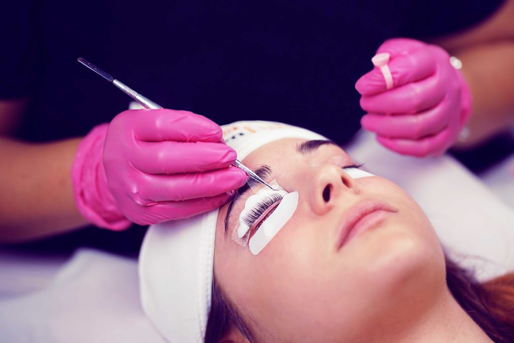 viso ragazza sdraiata con fascia in fronte e operatrice che esegue laminazione ciglia